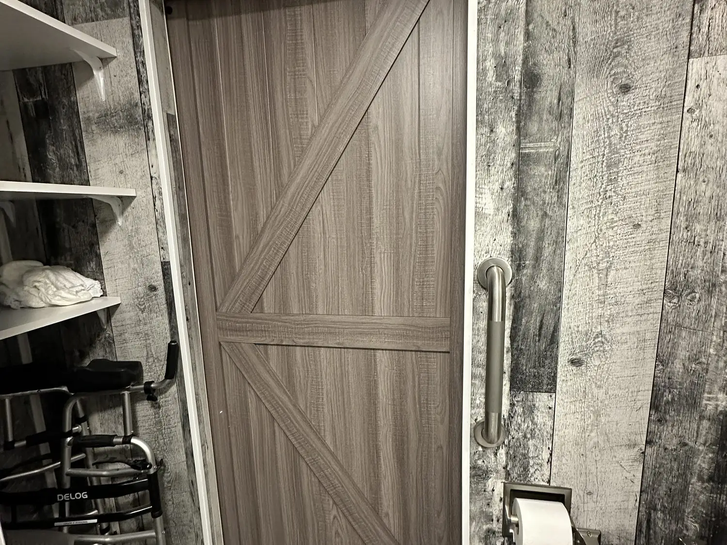 Remodeled accessible bathroom with rustic plank walls, barn door, and grab bars