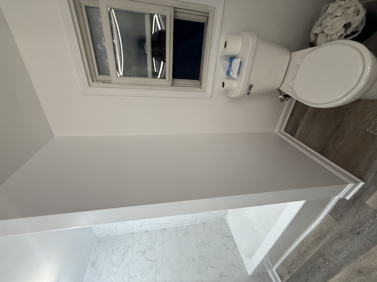 Finished bathroom with white marble tile tub surround and new wood-look flooring