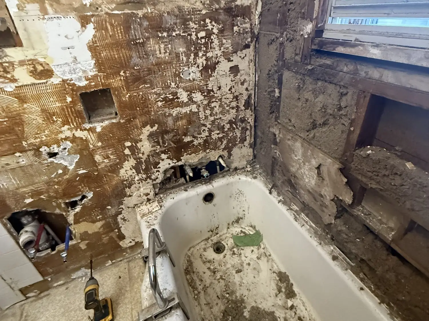 Bathroom stripped to the studs during demolition, old tub and window exposed