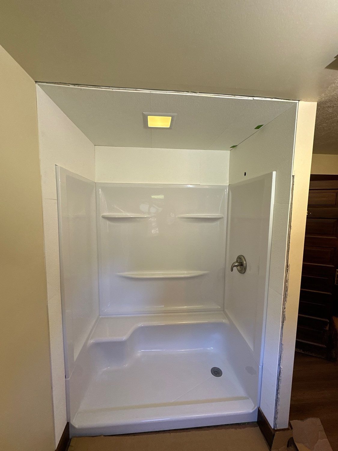 New white shower base and surround set level in the rebuilt alcove