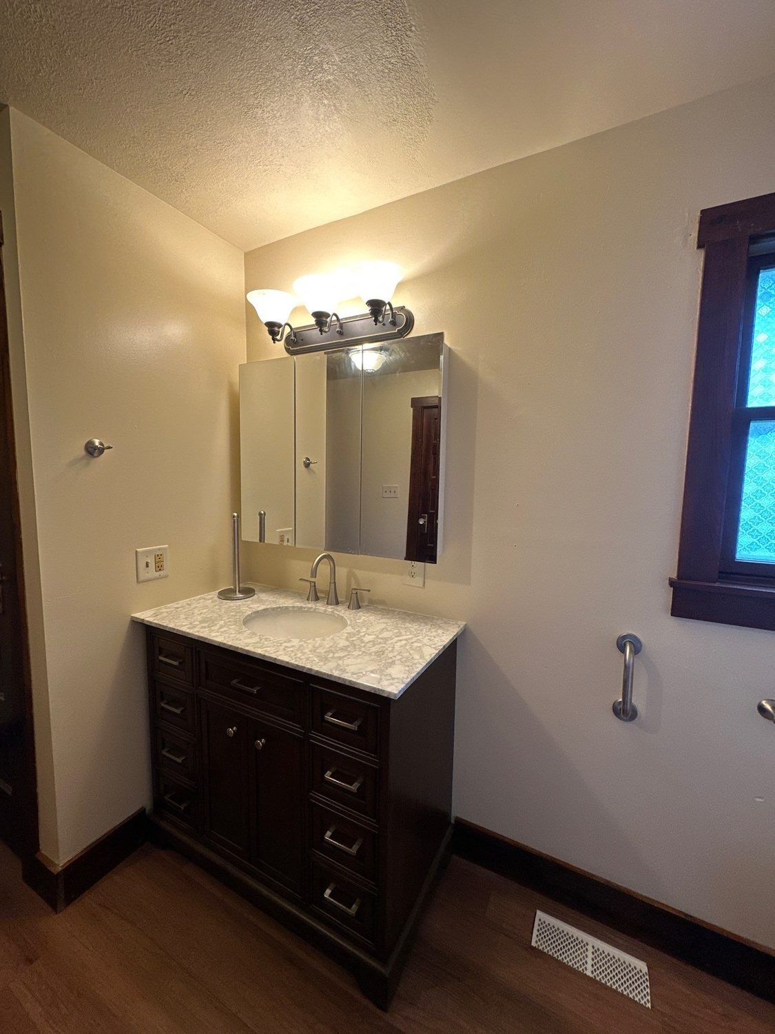 Dark wood vanity with a marble-look top, framed mirror, and grab bar in a New Hampshire, Ohio bathroom