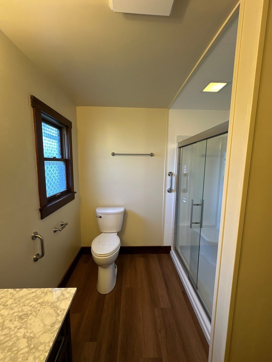 Comfort-height toilet with a wall grab bar beside a glass-door walk-in shower