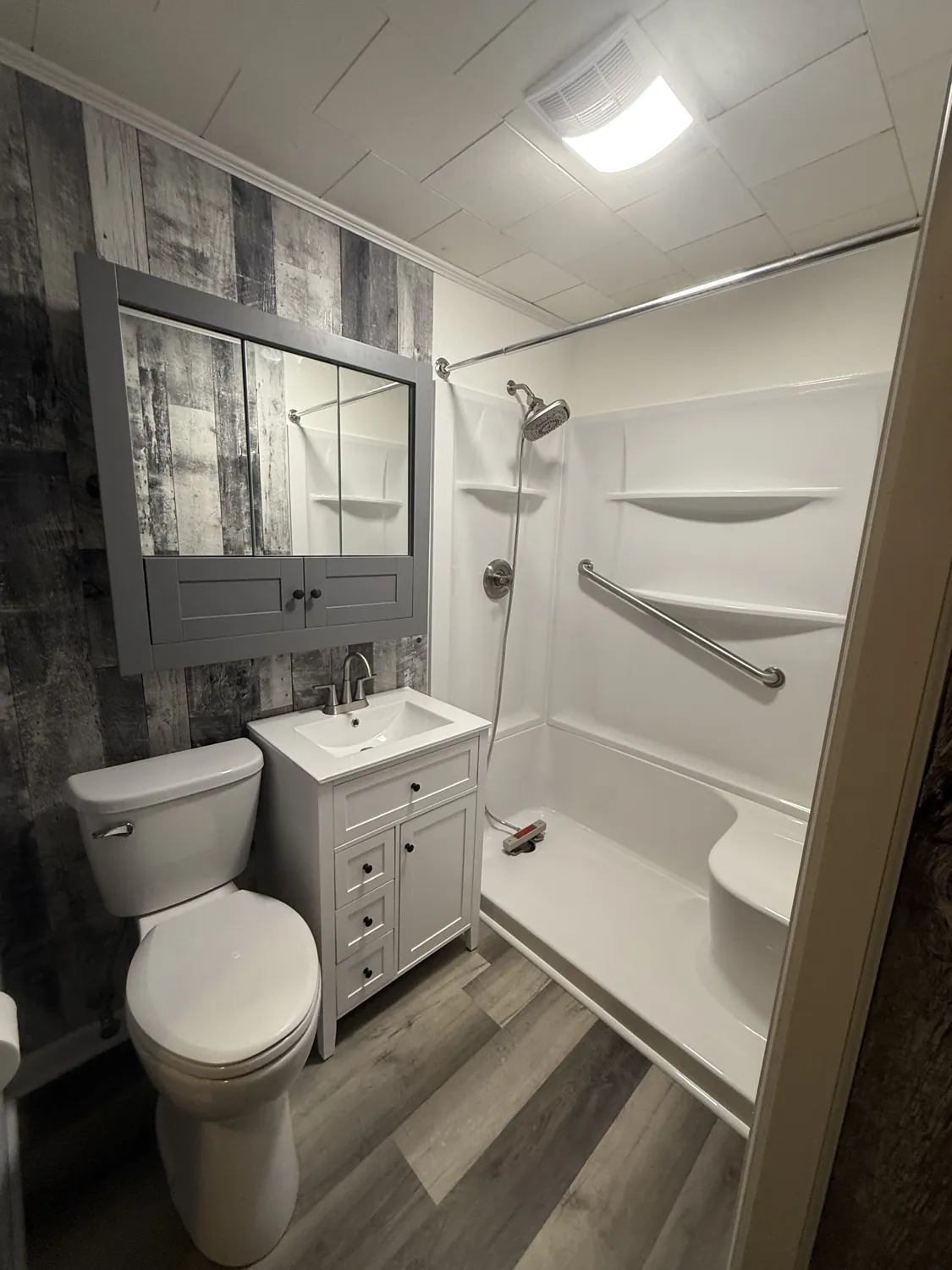 Completed bathroom remodel by Say When Contracting — gray vanity, walk-in shower with grab bars, and rustic accent wall in Lima, Ohio