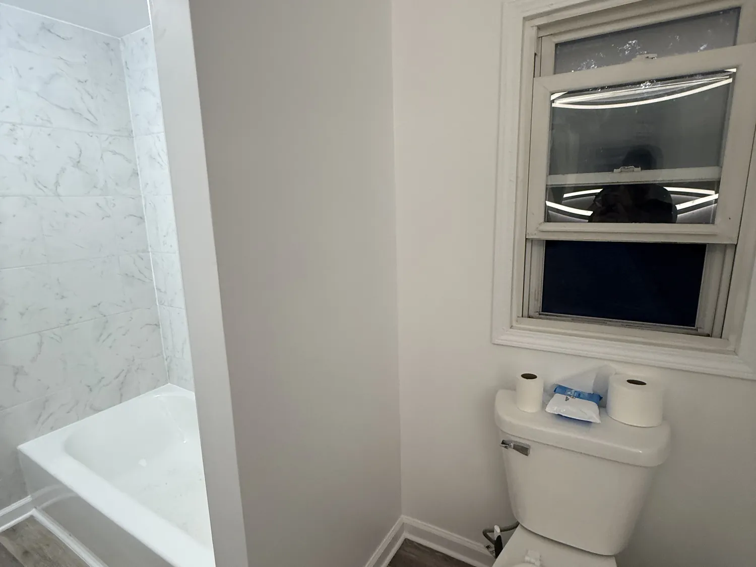 Rebuilt bathroom with a white marble-look tile tub surround, fresh drywall, and a new window