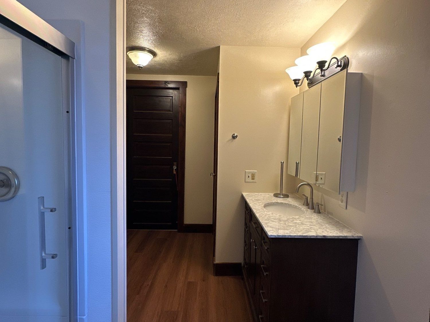 Rebuilt bathroom with a glass-door shower, dark wood vanity, and plank flooring, with the home's original stained trim kept intact