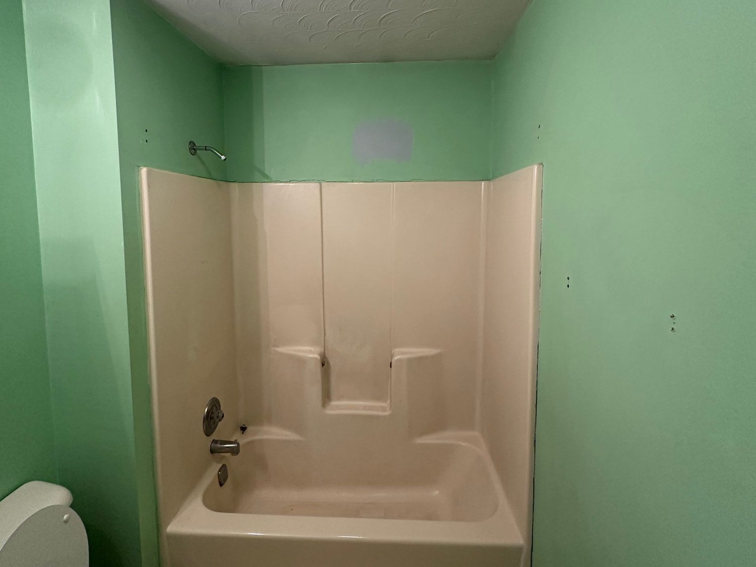 Dated bathroom in St. Marys, Ohio before remodeling, with a worn almond tub-shower unit and mint green walls